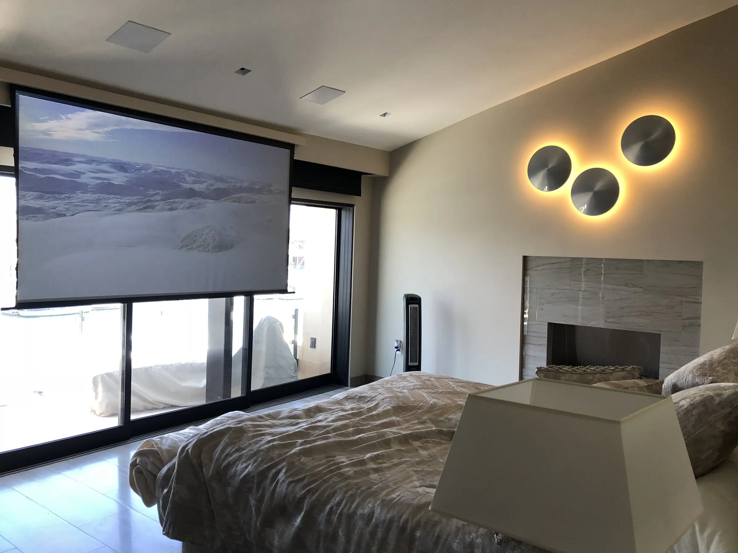 Bedroom with a projection screen lowered in front of glass doors beside a fireplace