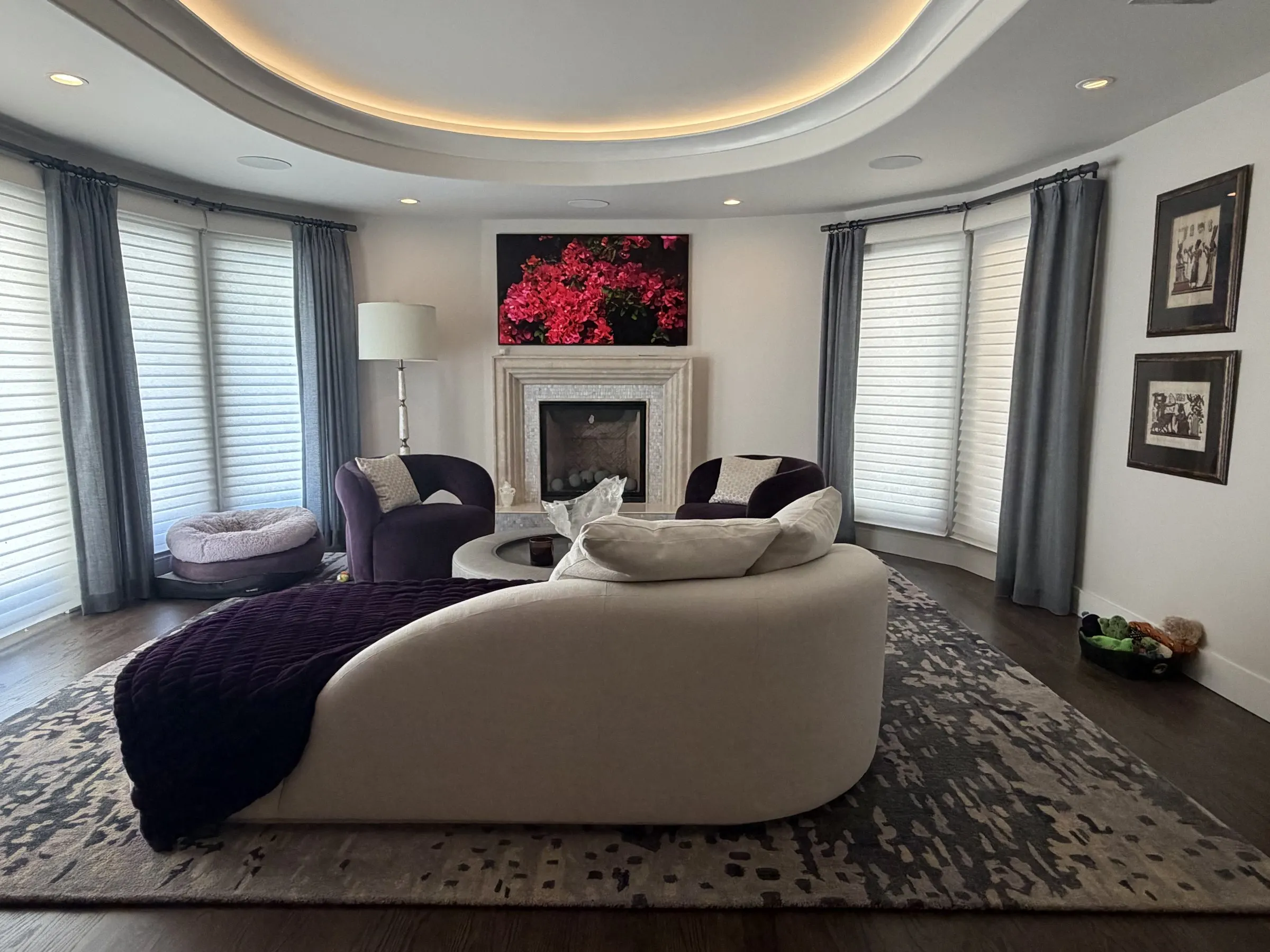 Living room with a lit circular ceiling cove, sheer shades, and a curved sofa facing the fireplace