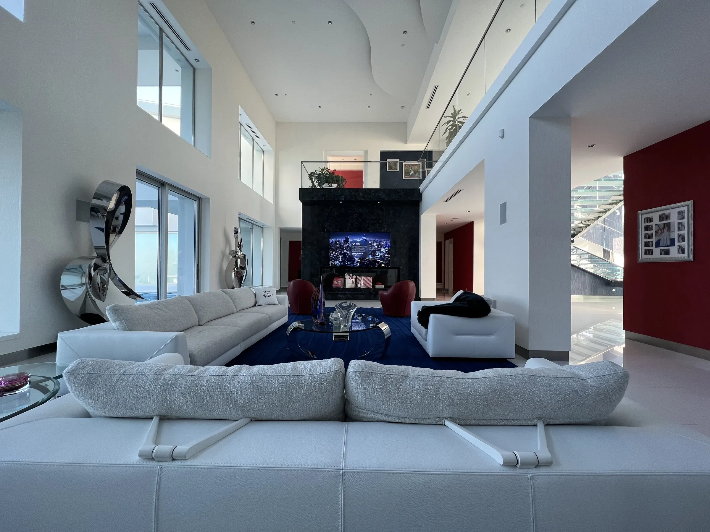 Double-height living room with white sofas facing a stone media wall