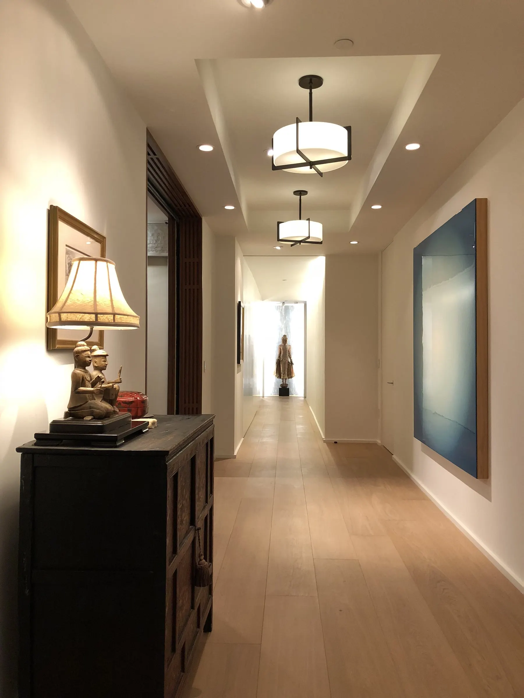 Long hallway with pendant lights, recessed lights, and lit artwork