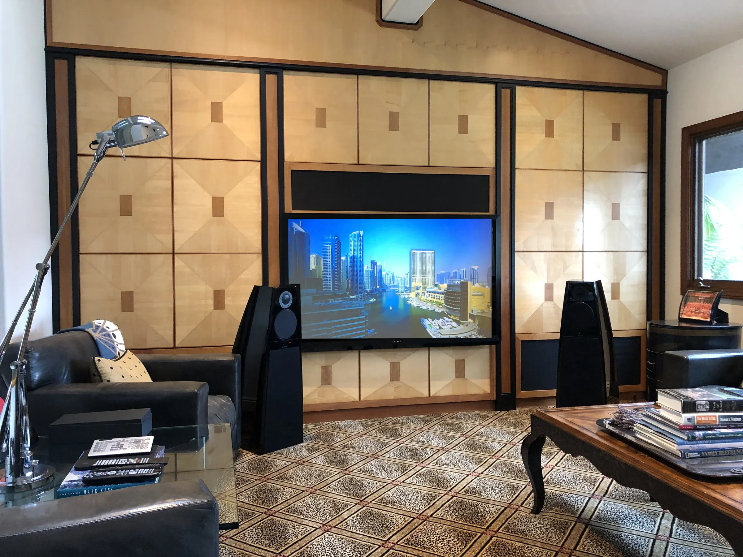 Wide view of a living room with black tower speakers flanking a display set into maple and walnut paneling