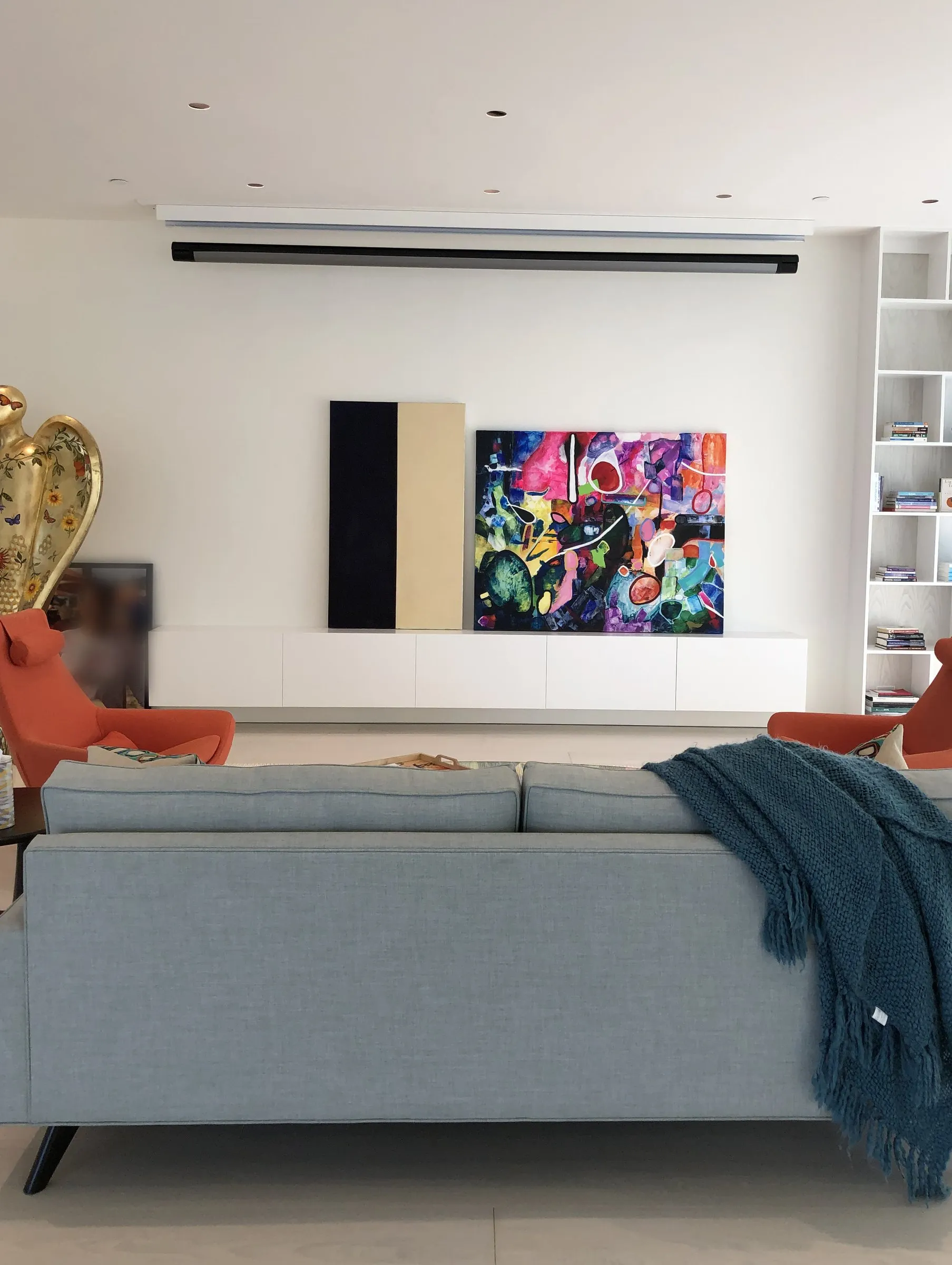 Bright living room with a colorful painting on a white wall, a projection screen hidden in the ceiling above