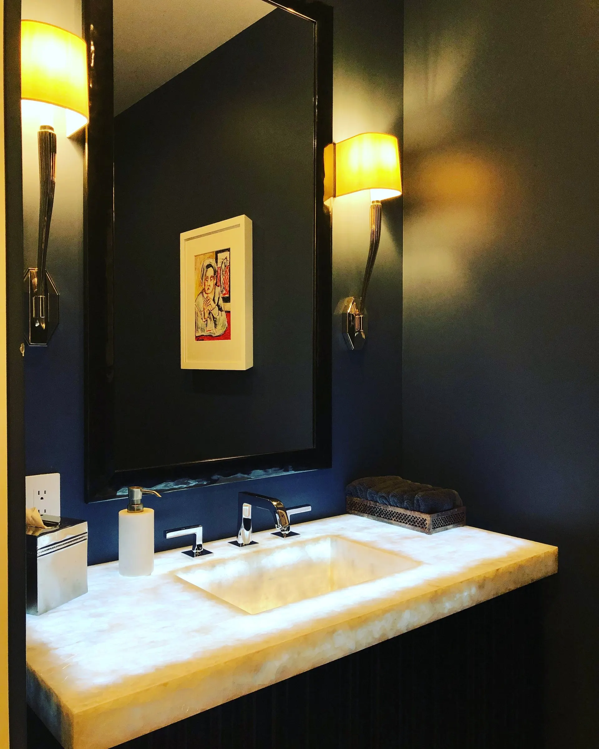 Powder room with brass sconces and an onyx sink, warmly lit
