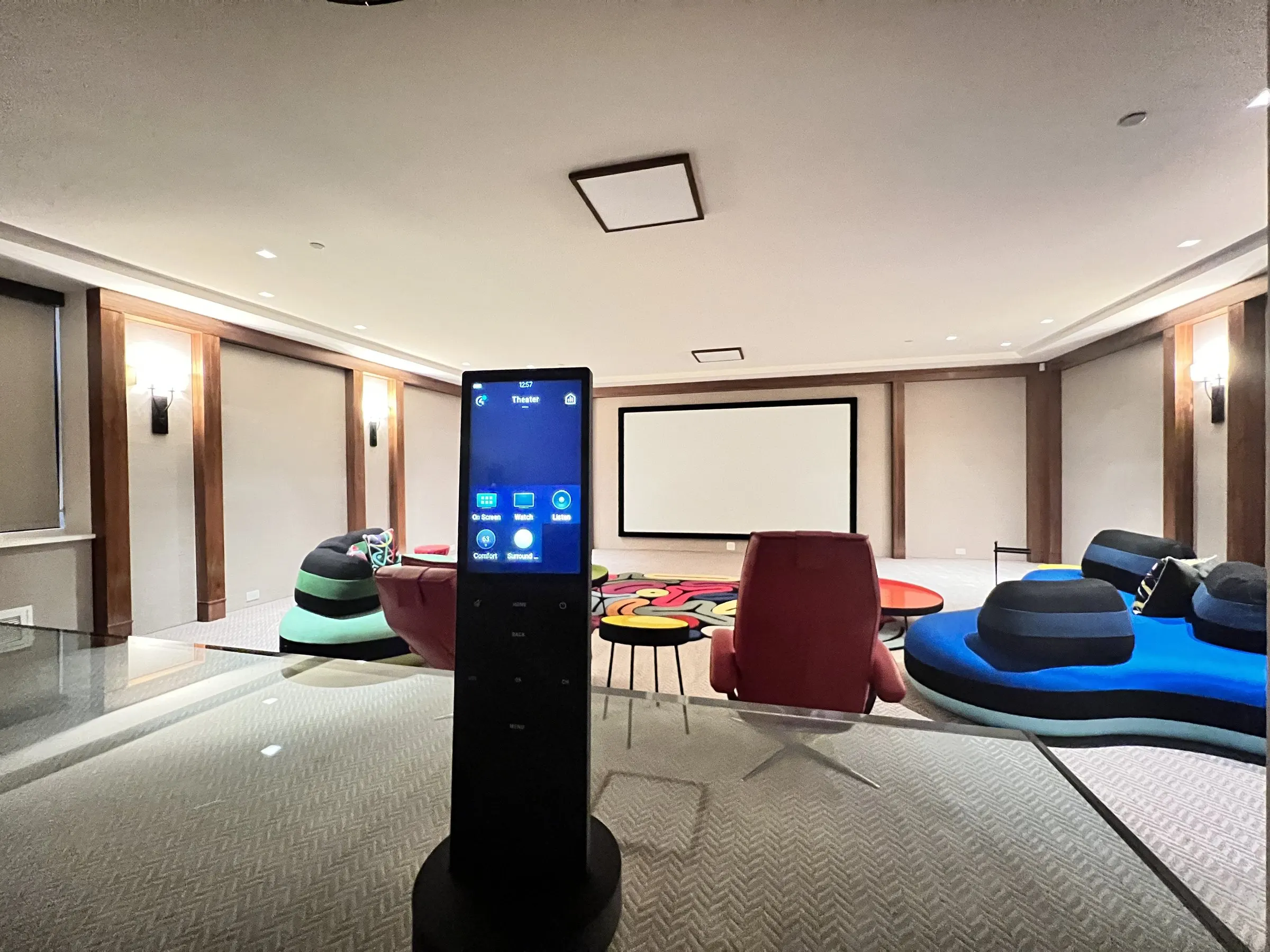 Handheld touchscreen remote in the foreground of a lounge theater with colorful seating