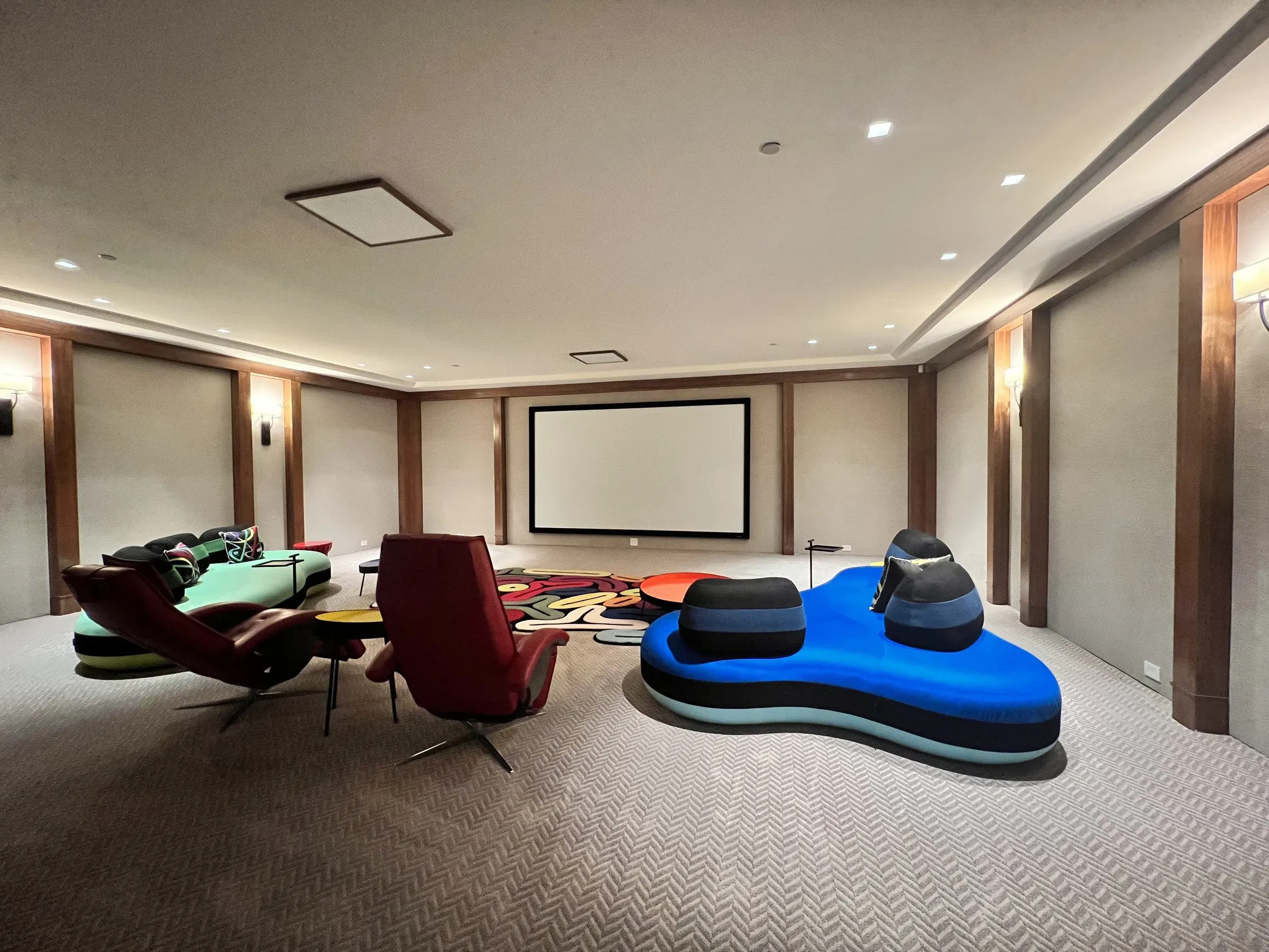 Wide view of a lounge theater with sculptural blue and green seating, wall sconces, and a projection screen