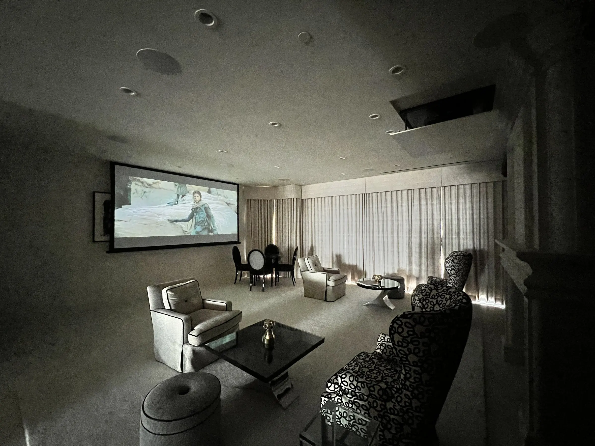 The same living room darkened with drapes closed and a film on the projection screen